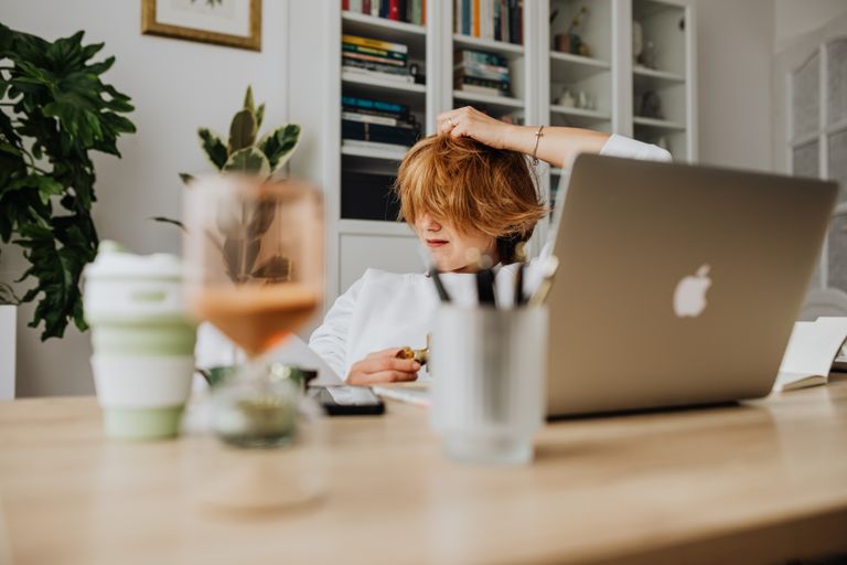 A relaxed home office setup with a woman using a laptop, surrounded by books and plants.
